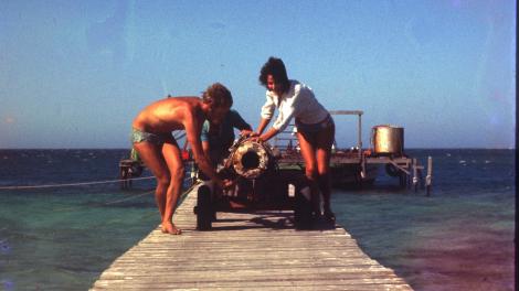 Two men rolling a cannon down a long wooden pier